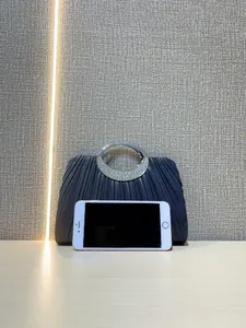 Detail of navy pleated evening clutch with rhinestone handle and smartphone size reference