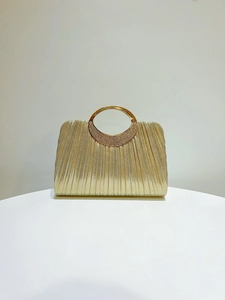 Close-up of golden pleated evening bag with sparkling crystal-embellished ring handle