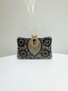 Detailed close-up of a luxury evening clutch with black rhinestones and golden hardware