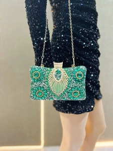 Close-up of luxury emerald floral rhinestone clutch with gold chain on evening dress