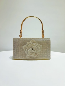 Detail of golden evening bag featuring 3D rhinestone rose and metallic ring handle