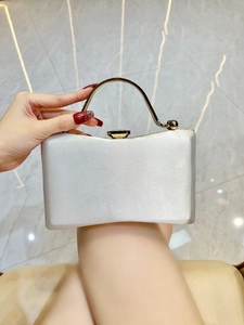 Close-up of white satin evening clutch with gold metal handle and dark gemstone clasp