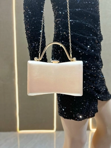 Detail of champagne satin evening clutch bag with gold metal handle and long chain strap