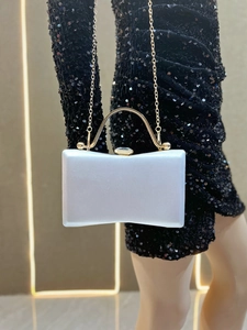Detail of evening clutch with satin fabric, gold metal handle, and gem clasp on black dress