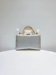 Detailed view of elegant silver satin clutch bag with curved golden metal handle