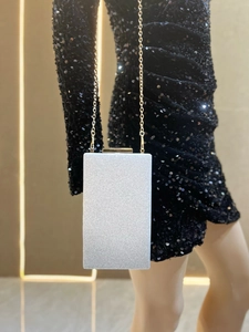 Pochette argentée pailletée avec chaîne dorée présentée sur mannequin en robe à paillettes