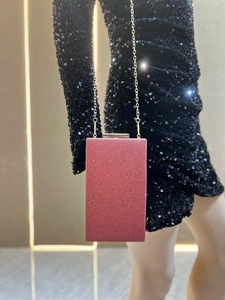 Détail d'une pochette de soirée rouge pailletée avec chaîne dorée portée sur une robe noire