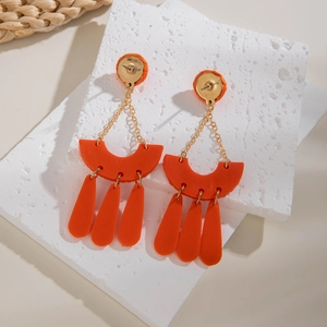 Bohemian orange clay earrings with geometric fringe and gold chains on stone display