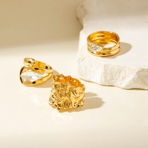 Trois bagues dorées avec pierres marquise et texture lave sur fond de pierre