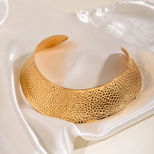 Collier choker large en métal doré martelé présenté sur un tissu en soie blanche