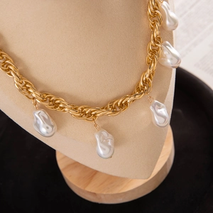 Detail of chunky gold chain necklace with white baroque pearl pendants on beige bust