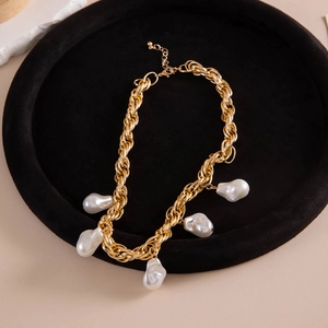 Close-up of golden chunky chain necklace with five white baroque pearls on black velvet