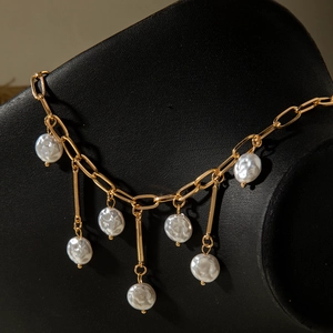 Close-up of gold chain necklace featuring baroque pearls on a black jewelry bust