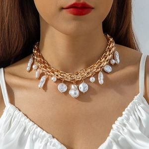 Detail of chunky gold chain necklace with baroque pearls on a white silk dress