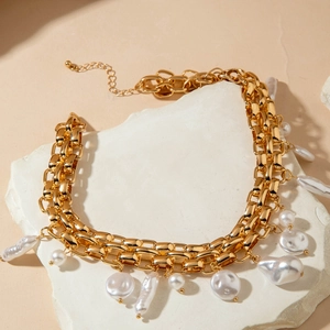 Detail of chunky gold chain necklace featuring natural baroque pearls on a stone texture