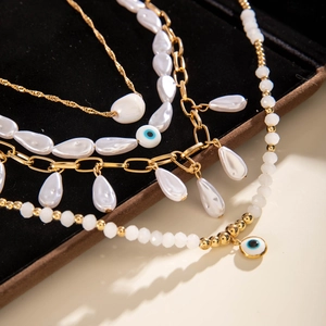 Detail of layered gold chains with evil eye charm and pearl pendants on black velvet