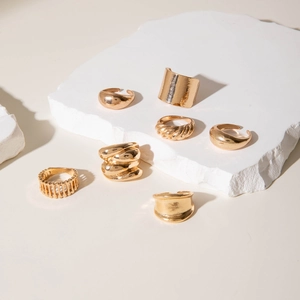 Set di 7 anelli dorati con varie trame su sfondo di pietra minimalista dal design moderno