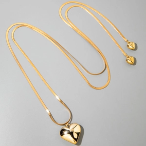 Detalle de un collar con colgante de corazón dorado y cadena de serpiente sobre gris
