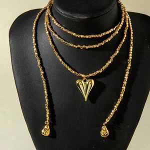 Detalle de collar multicapa de cuentas doradas con colgante de corazón pulido de espejo