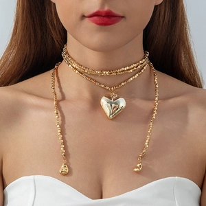 Detalle de gargantilla dorada de varias capas con colgante de corazón y borlas largas