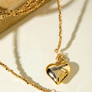 Primer plano de un collar dorado con colgante de corazón y cadena de cuentas cuadradas