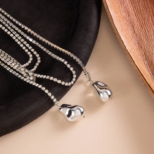 Collar de varias capas con pedrería y colgantes de gota plateados en fondo chic
