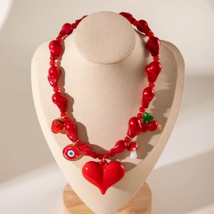 Détail d'un collier de perles rouges avec breloques cœur, fraise et œil sur buste