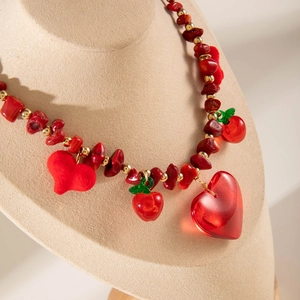 Détail d'un collier de perles rouges avec pendentifs cœur et breloques pomme sur support