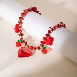 Gros plan d'un collier de perles rouges avec breloques cœur et cerise sur support blanc