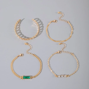 Detail of four-piece gold bracelet set featuring green gems and twisted rope chain design