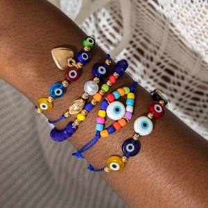 Detail of stacked bohemian evil eye beaded bracelets with gold heart and shell charms