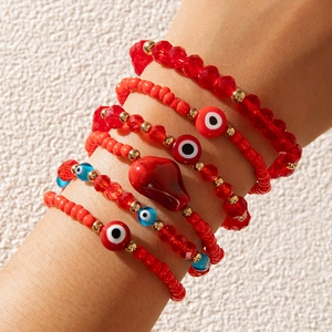 Detail shot of multi-layer red beaded bracelets set with evil eye and heart charms