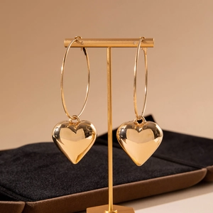 Elegant gold hollow hoop earrings with 3D heart-shaped charms on display stand
