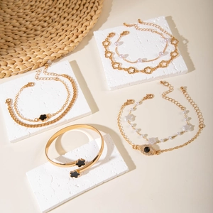 Golden jewelry set with floral charms, faux pearls and evil eye bracelets on white boards