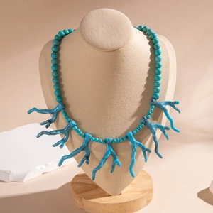 Détail du collier bohème turquoise en forme de corail sur un présentoir beige