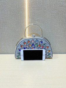 Detailed view of peacock rhinestone evening bag size compared with a white smartphone