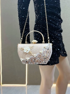 Détail de pochette de soirée avec fleurs blanches, perles et texture de paillettes dorées