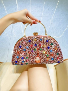 Detail of peacock rhinestone evening bag with red base and gold curved handle