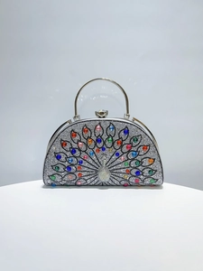 Macro detail of a peacock clutch bag featuring vibrant rhinestones and a metal handle