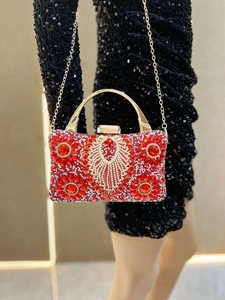 Detail of red crystal evening bag with gold handle held against a black sequin dress