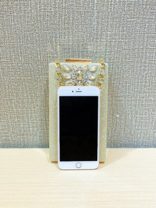 Golden evening clutch with crystal flower detail and metal chain, size compared to phone