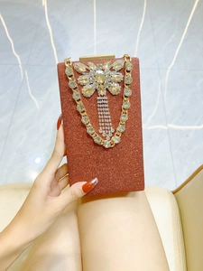 Detail of copper-orange glitter evening clutch featuring a rhinestone butterfly and gold chain