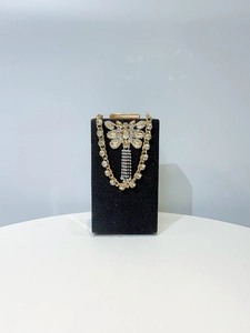 Detail of black evening bag featuring golden butterfly crystal tassel and metal chain