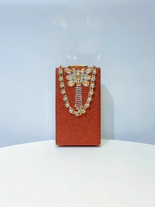Macro detail of red glitter clutch with rhinestone bow and gold chain strap