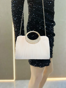 Detail of white pleated evening clutch with crystal-encrusted gold ring handle and chain