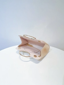 Detail view of cream straw evening bag with golden ring handles and chain strap