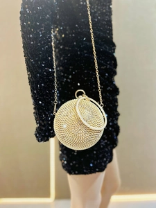 Detail of a gold spherical evening bag with rhinestones and round handle on a model
