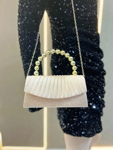 Detail of champagne gold evening clutch featuring pleated fabric and pearl top handle