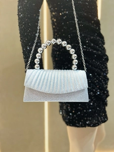 Detail of silver pleated evening clutch with pearl handle and chain on black sequin dress