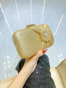 Sparkling gold glitter clutch bag with rhinestone flower held against black dress